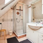 Badezimmer mit Dusche, Waschbecken mit großem Spiegel, Haarföhn und Abstellplatz