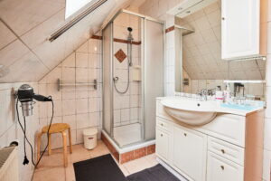 Badezimmer mit Dusche, Waschbecken mit großem Spiegel, Haarföhn und Abstellplatz