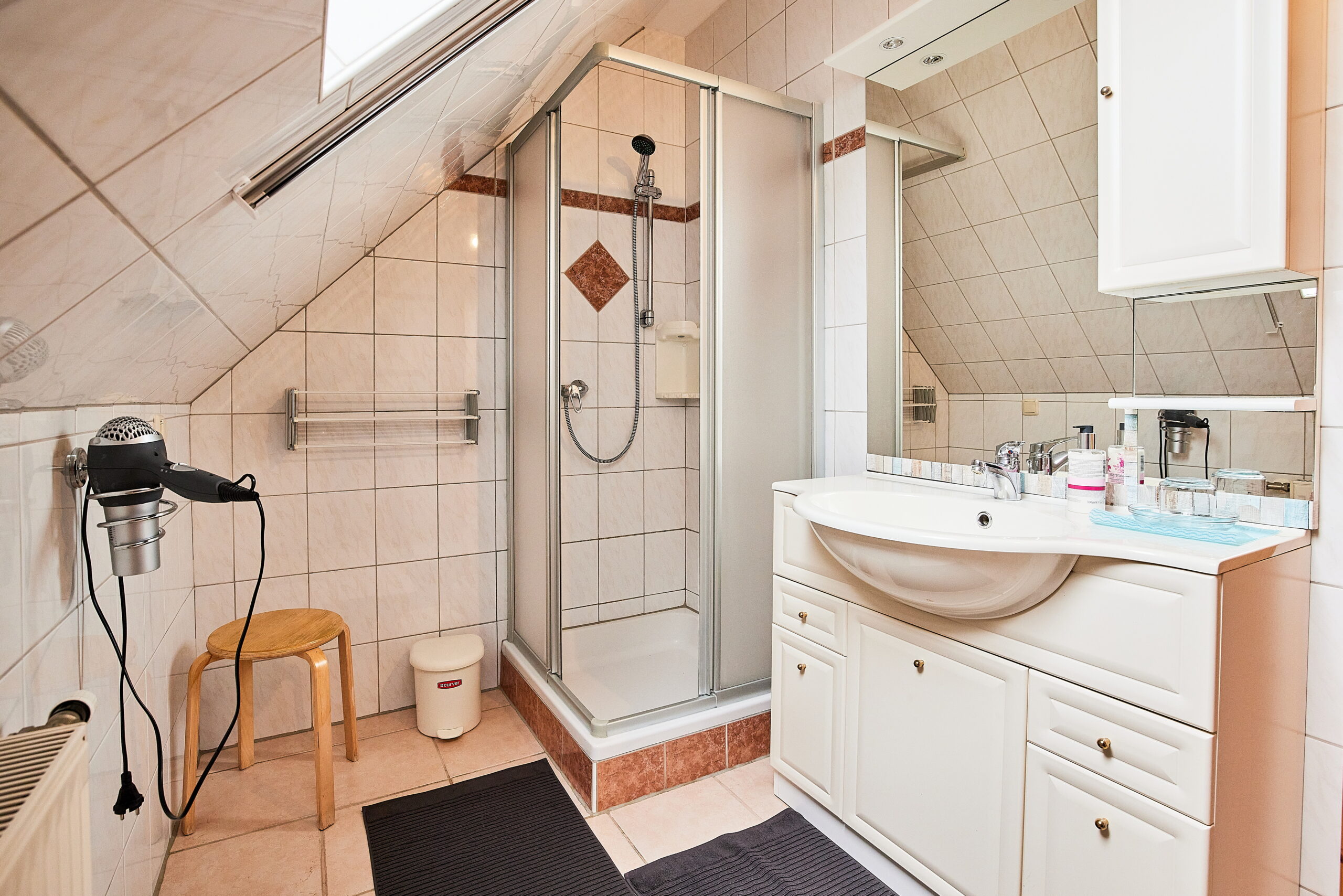 Badezimmer mit Dusche, Waschbecken mit großem Spiegel, Haarföhn und Abstellplatz